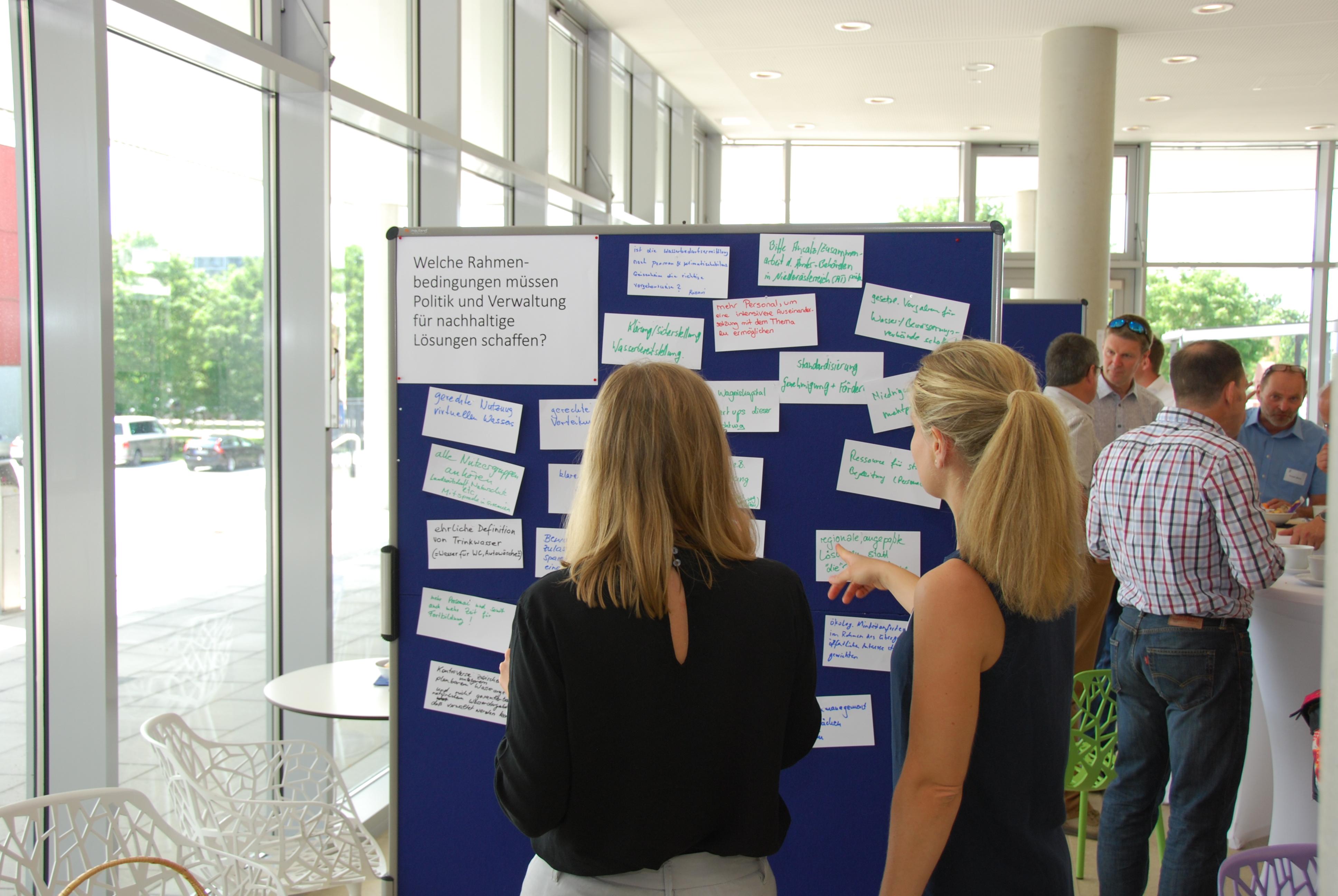 Two female participants in front of a pin-board with a collection of ideas for sustainable water management.
