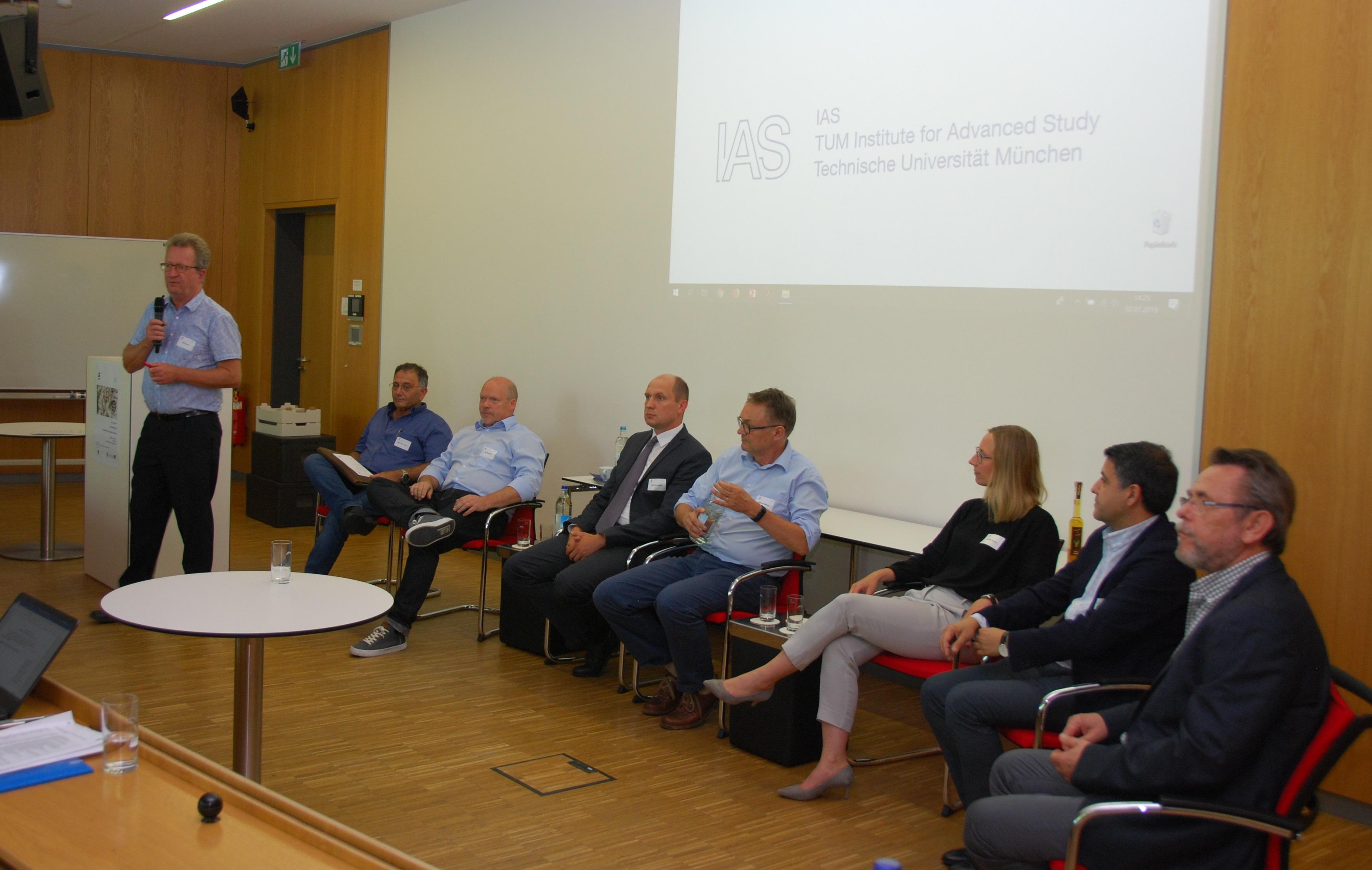 Eight discussants in front of the audience with the logo of TUM-IAS in the background.